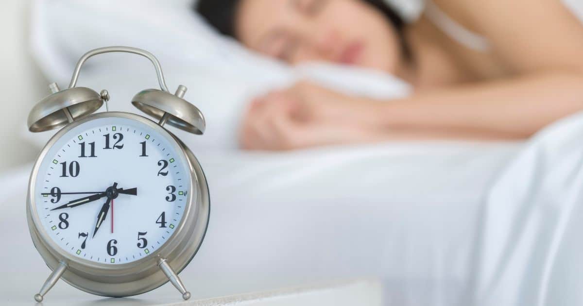 woman sleeping with alarm clock next to bed